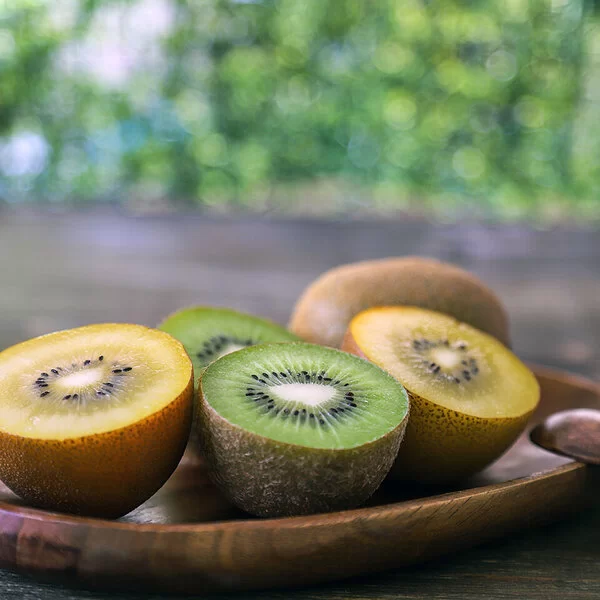 Auf einer Holzschale liegen aufgeschnittene gelbe und grüne Kiwis.