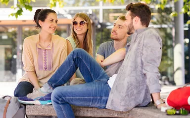 Zwei junge Frauen und zwei Junge Männer sitzen im Freien unter einem Baum. Auch als Studierende sind sie bei der AOK gut versichert.