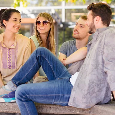 Zwei junge Frauen und zwei Junge Männer sitzen im Freien unter einem Baum. Auch als Studierende sind sie bei der AOK gut versichert.