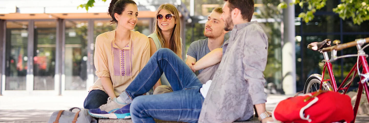 Zwei junge Frauen und zwei Junge Männer sitzen im Freien unter einem Baum. Auch als Studierende sind sie bei der AOK gut versichert.