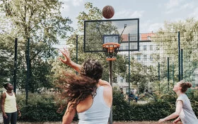 Drei Frauen treiben draußen gemeinsam Sport und spielen Basketball.