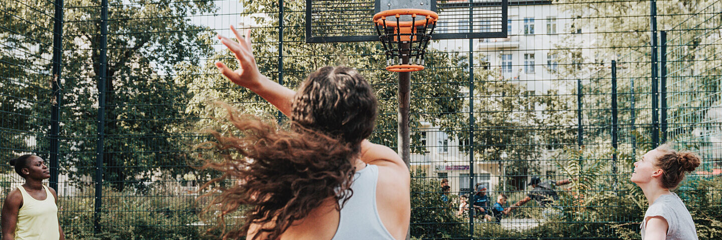 Drei Frauen treiben draußen gemeinsam Sport und spielen Basketball.