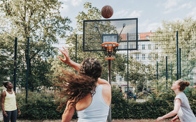 Drei Frauen treiben draußen gemeinsam Sport und spielen Basketball.