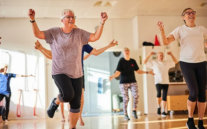 Gruppe von Seniorinnen und Senioren, die lächelnd bei einem Fitnesskurs mitmachen.