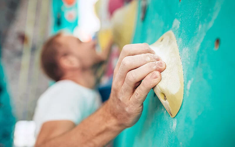 Mann beim Bouldern in einer Boulderhalle hält sich an Griff fest.