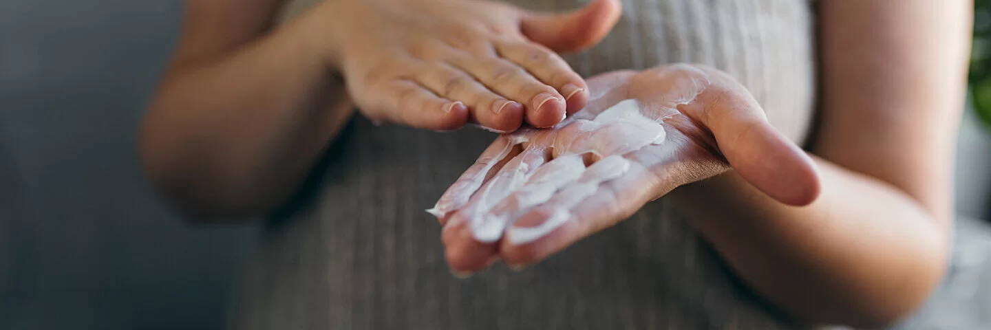 Eine Frau mit Diabetes, die unter trockener Haut leidet, verreibt Creme in ihren Händen.