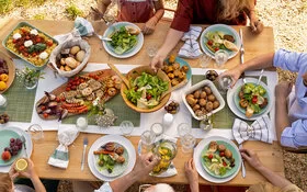 Mehrere Menschen sitzen draußen an einem reich gedeckten Tisch und essen gemeinsam.
