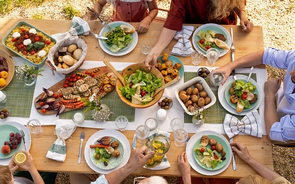 Mehrere Menschen sitzen draußen an einem reich gedeckten Tisch und essen gemeinsam.