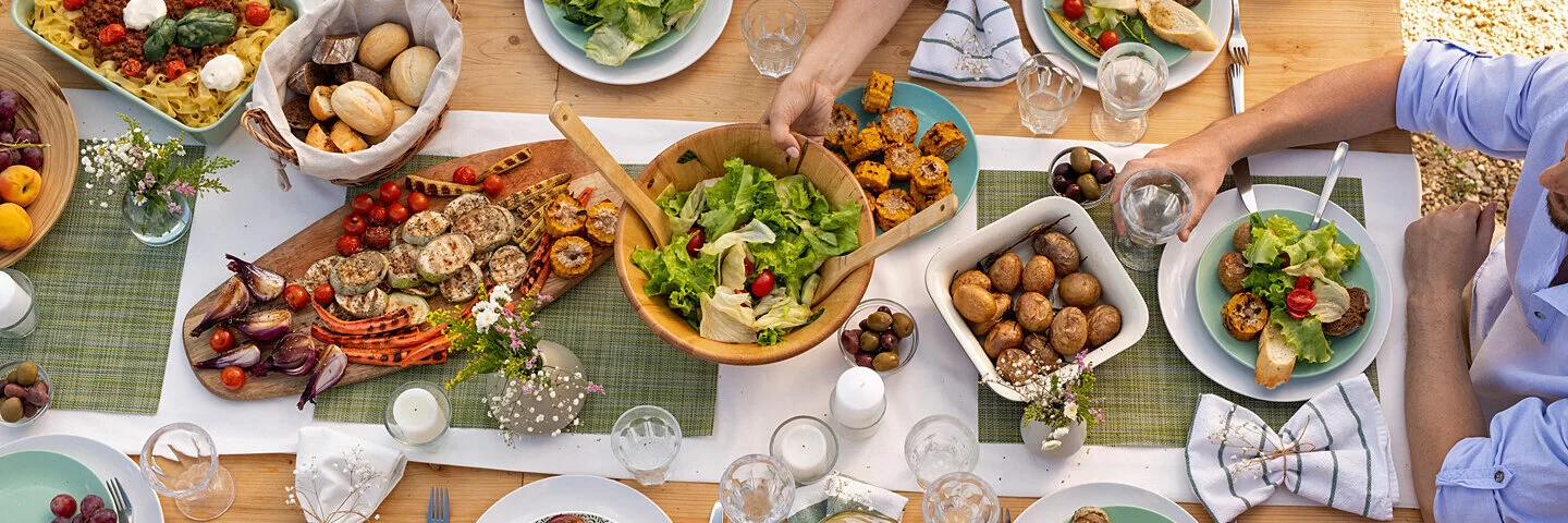 Mehrere Menschen sitzen draußen an einem reich gedeckten Tisch und essen gemeinsam.