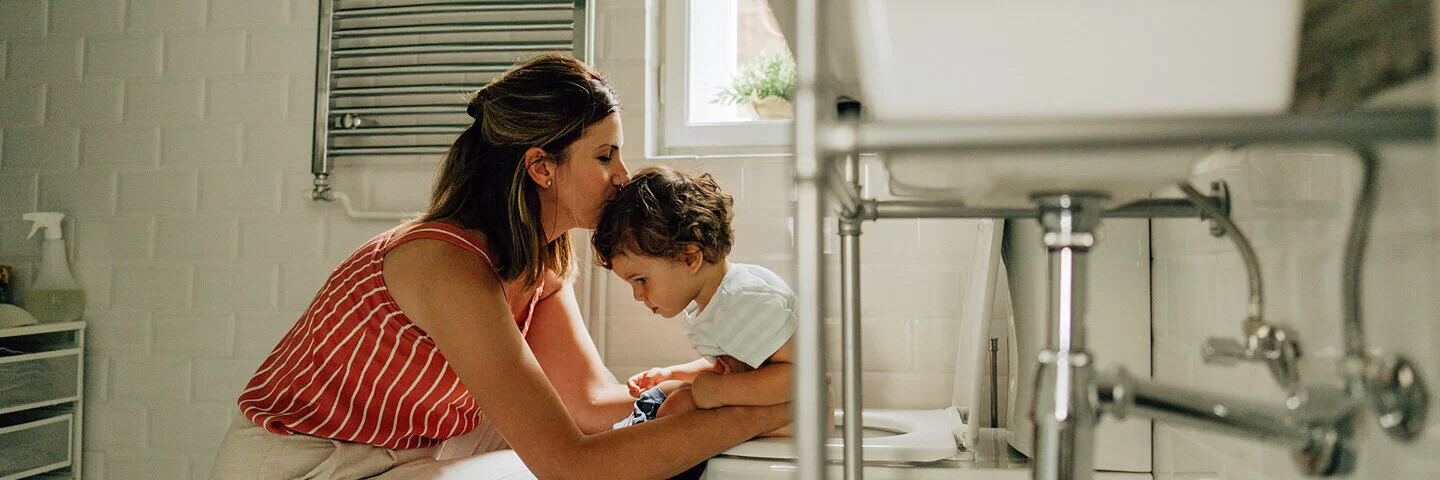 Mutter unterstützt ihr kleines Kind, das unter einer Verstopfung leidet, beim Toilettengang.