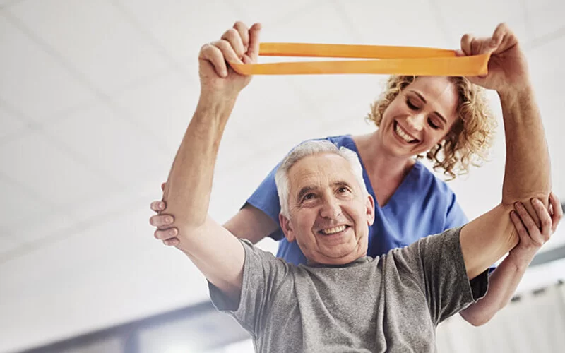 Eine Physiotherapeutin macht Übungen mit einem älteren Patienten mit einem Gymnastikband.