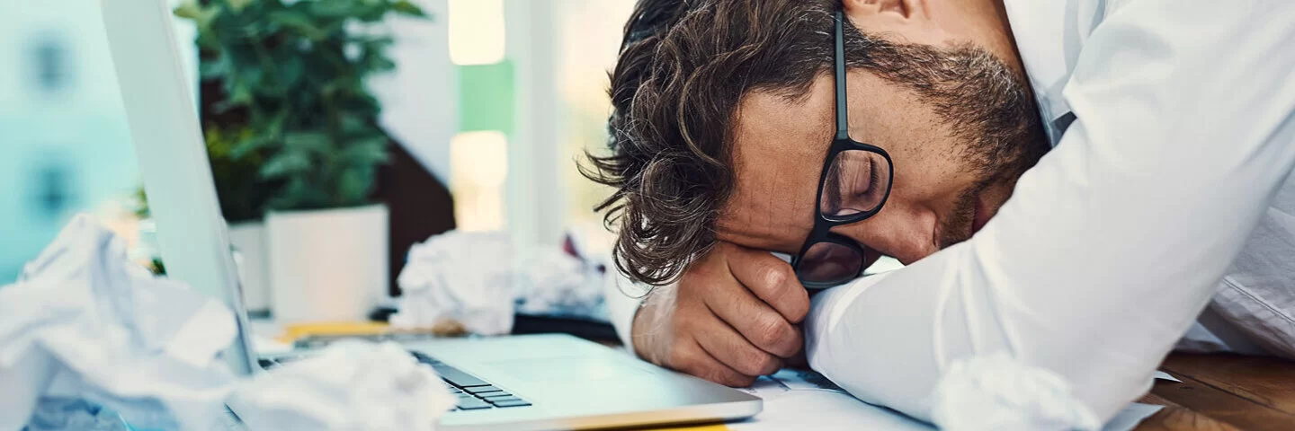 Mann macht ein Powernap auf seinem Schreibtisch, um neue Energie zu tanken.