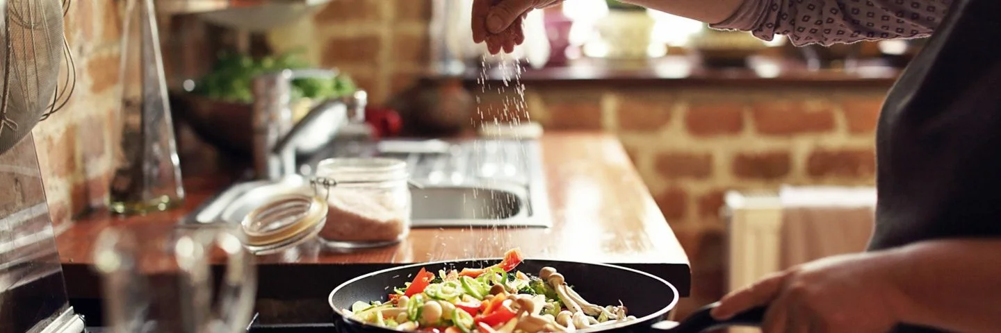 Eine Gemüsepfanne auf dem Herd wird mit Jodsalz gewürzt.