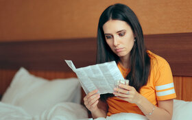 Eine junge Frau sitzt im Bett und schaut auf einen Beipackzettel, den sie in den Händen hält.