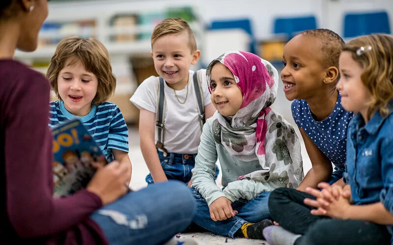 Eine Erzieherin in einer Kita zeigt fünf Kindern ein aufgeschlagenes Buch.