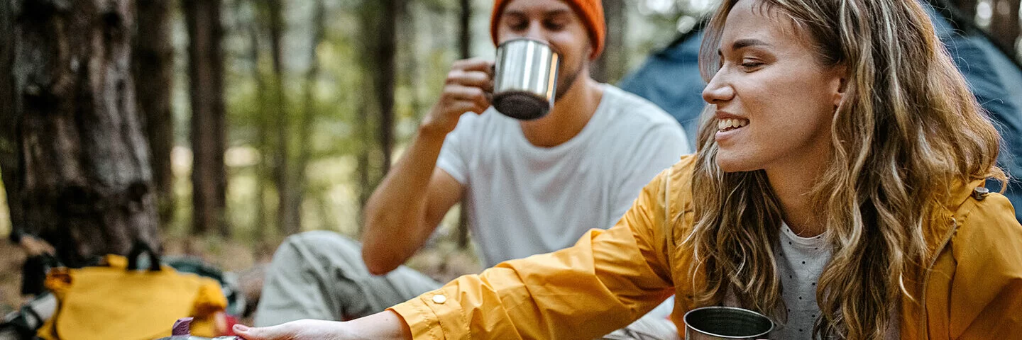 Ein Mann und eine Frau campen und kochen Kaffee im Wald.