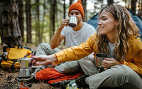 Ein Mann und eine Frau campen und kochen Kaffee im Wald.