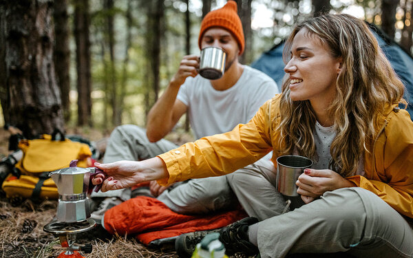 Ein Mann und eine Frau campen und kochen Kaffee im Wald.
