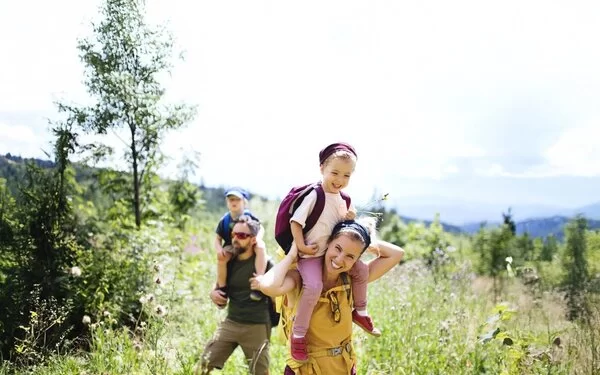 Junge Familie mi Kindern auf den Schultern wandern durch eine Wildkräuterwiese 