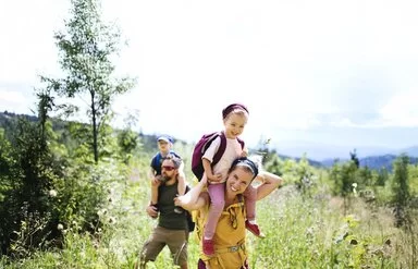 Junge Familie mi Kindern auf den Schultern wandern durch eine Wildkräuterwiese 
