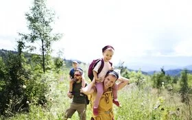 Junge Familie mi Kindern auf den Schultern wandern durch eine Wildkräuterwiese 