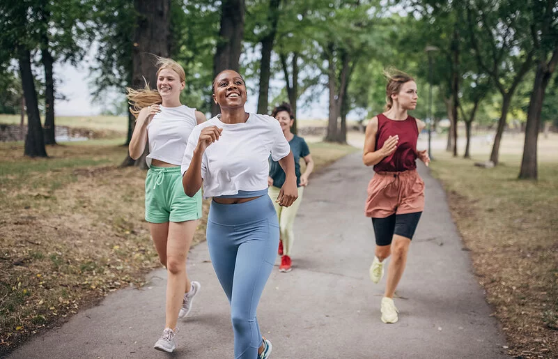 An einem Sommertag joggen vier Frauen in einem Park.