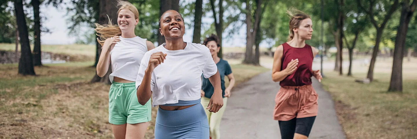 An einem Sommertag joggen vier Frauen in einem Park.