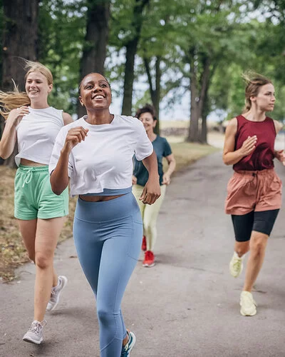 An einem Sommertag joggen vier Frauen in einem Park.
