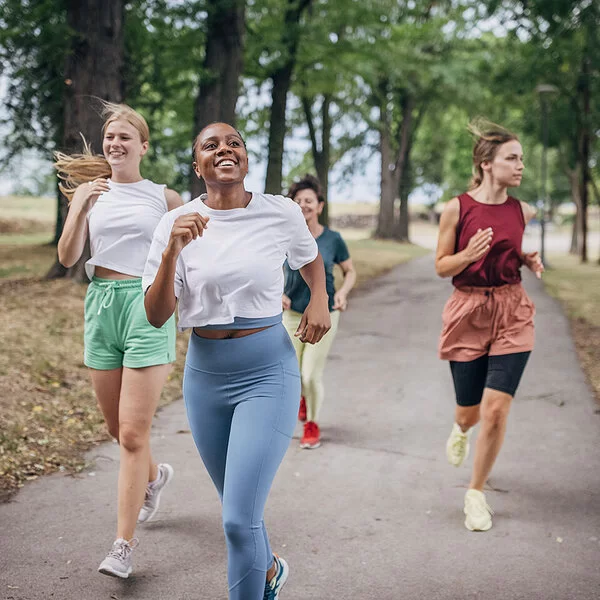 An einem Sommertag joggen vier Frauen in einem Park.