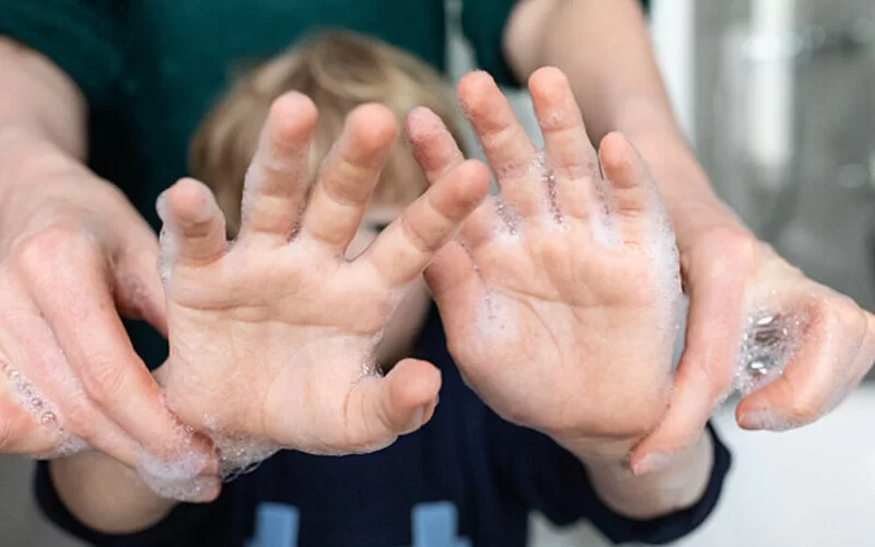 Vater und Sohn waschen sich die Hände, der Junge hält die eingeseiften Hände in die Kamera.