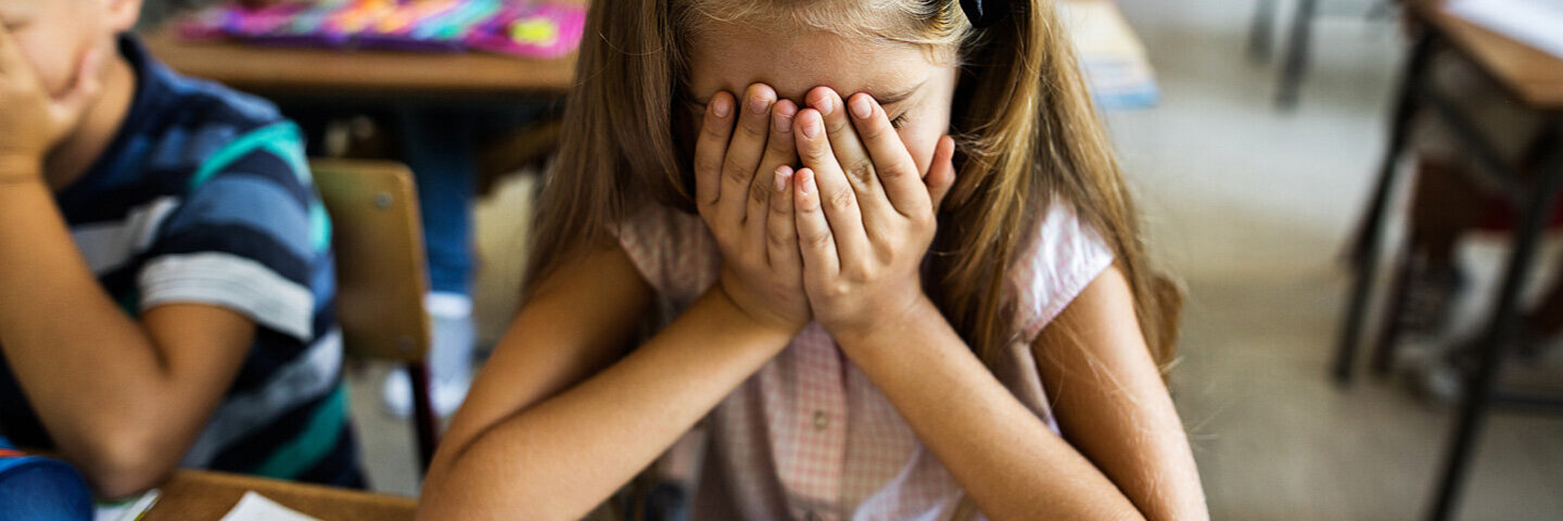 Ein Mädchen, welches Schulstress hat, hält sich die Hände an den Kopf.