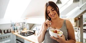 Schwangere Frau isst einen Salat und ernährt sich gesund, um auch in der Schwangerschaft auf ein gesundes Gewicht zu achten.