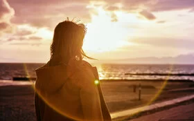 Eine Person steht an einem Strand und beobachtet den Sonnenaufgang.