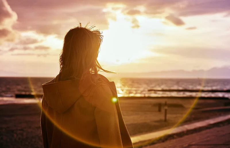 Eine Person steht an einem Strand und beobachtet den Sonnenaufgang.
