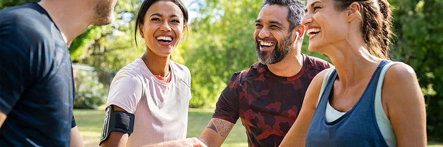 Zwei Männer und zwei Frauen stehen im Park lächelnd beisammen und legen die Hände übereinander. Die AOK-SportTreffs in Baden-Württemberg sind sehr beliebt.