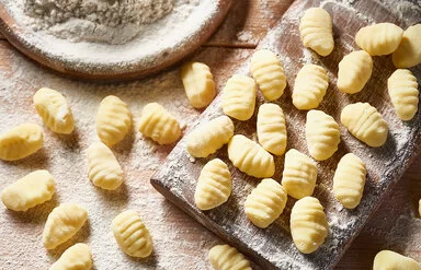 Auf einem mit Mehl bestäubtem Brett und einem Tisch liegen frisch zubereitete Gnocchi.