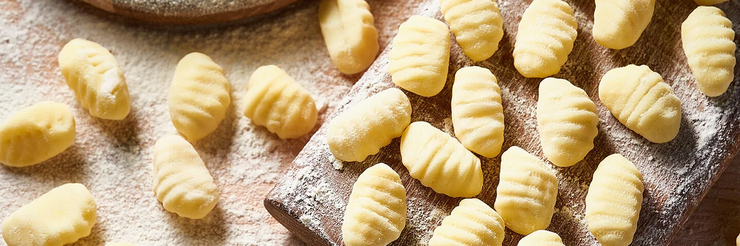 Auf einem mit Mehl bestäubtem Brett und einem Tisch liegen frisch zubereitete Gnocchi.