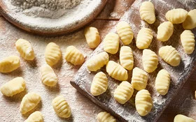 Auf einem mit Mehl bestäubtem Brett und einem Tisch liegen frisch zubereitete Gnocchi.