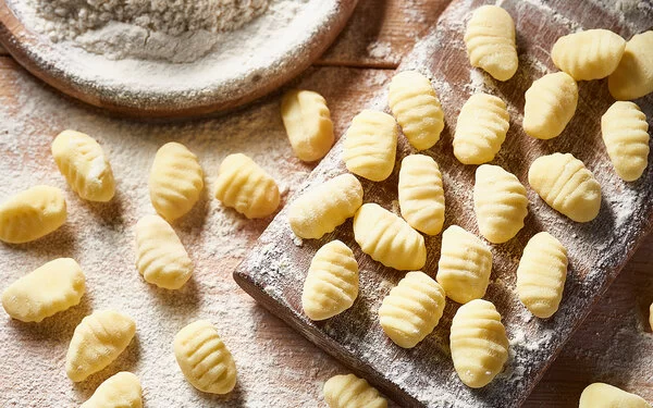Auf einem mit Mehl bestäubtem Brett und einem Tisch liegen frisch zubereitete Gnocchi.