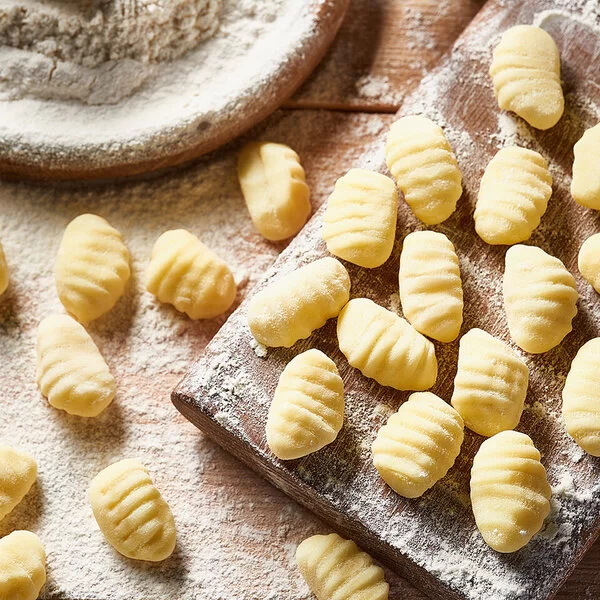 Auf einem mit Mehl bestäubtem Brett und einem Tisch liegen frisch zubereitete Gnocchi.