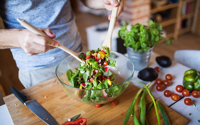 Jemand bereitet sich in der Küche einen Salat zu, darin enthaltene Ballaststoffe unterstützen die Verdauung.