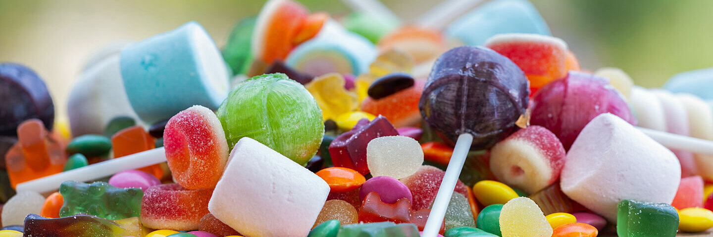 Auf einem Holzbrettchen liegt ein Haufen Süßigkeiten wie Lollis, Schokolinsen, Fruchtgummis und Marshmallows.