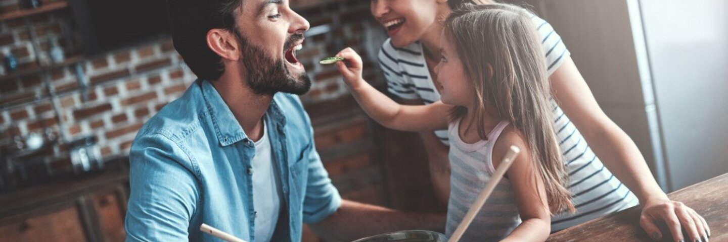 Gesunde Ernährung für Kinder: Mutter, Vater und Tochter bereiten gemeinsam einen Salat zu.