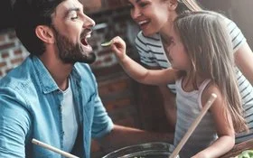 Gesunde Ernährung für Kinder: Mutter, Vater und Tochter bereiten gemeinsam einen Salat zu.
