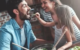 Gesunde Ernährung für Kinder: Mutter, Vater und Tochter bereiten gemeinsam einen Salat zu.