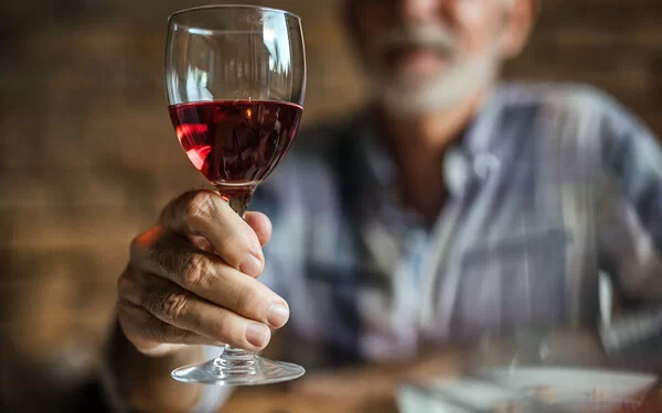 Ein älterer Mann hält ein Glas Rotwein in die Kamera.