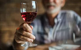 Ein älterer Mann hält ein Glas Rotwein in die Kamera.