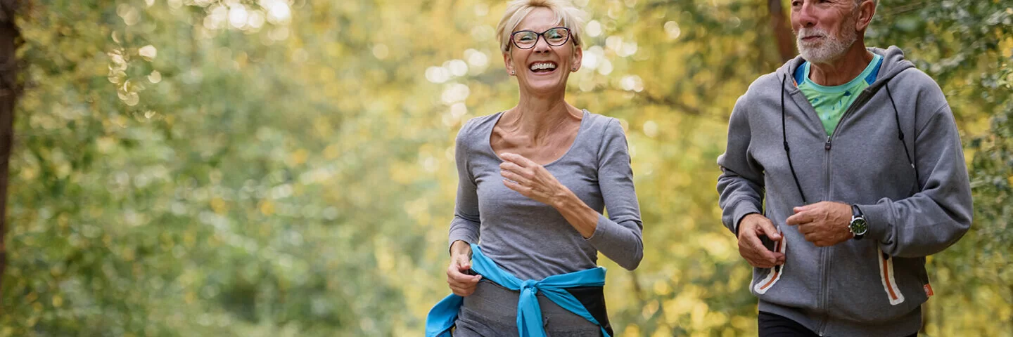 Aktives Seniorenpaar joggt gutgelaunt in einem Park.