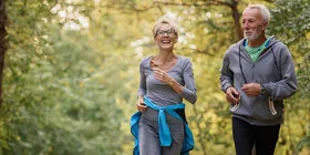 Aktives Seniorenpaar joggt gutgelaunt in einem Park.