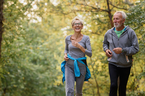 Aktives Seniorenpaar joggt gutgelaunt in einem Park.